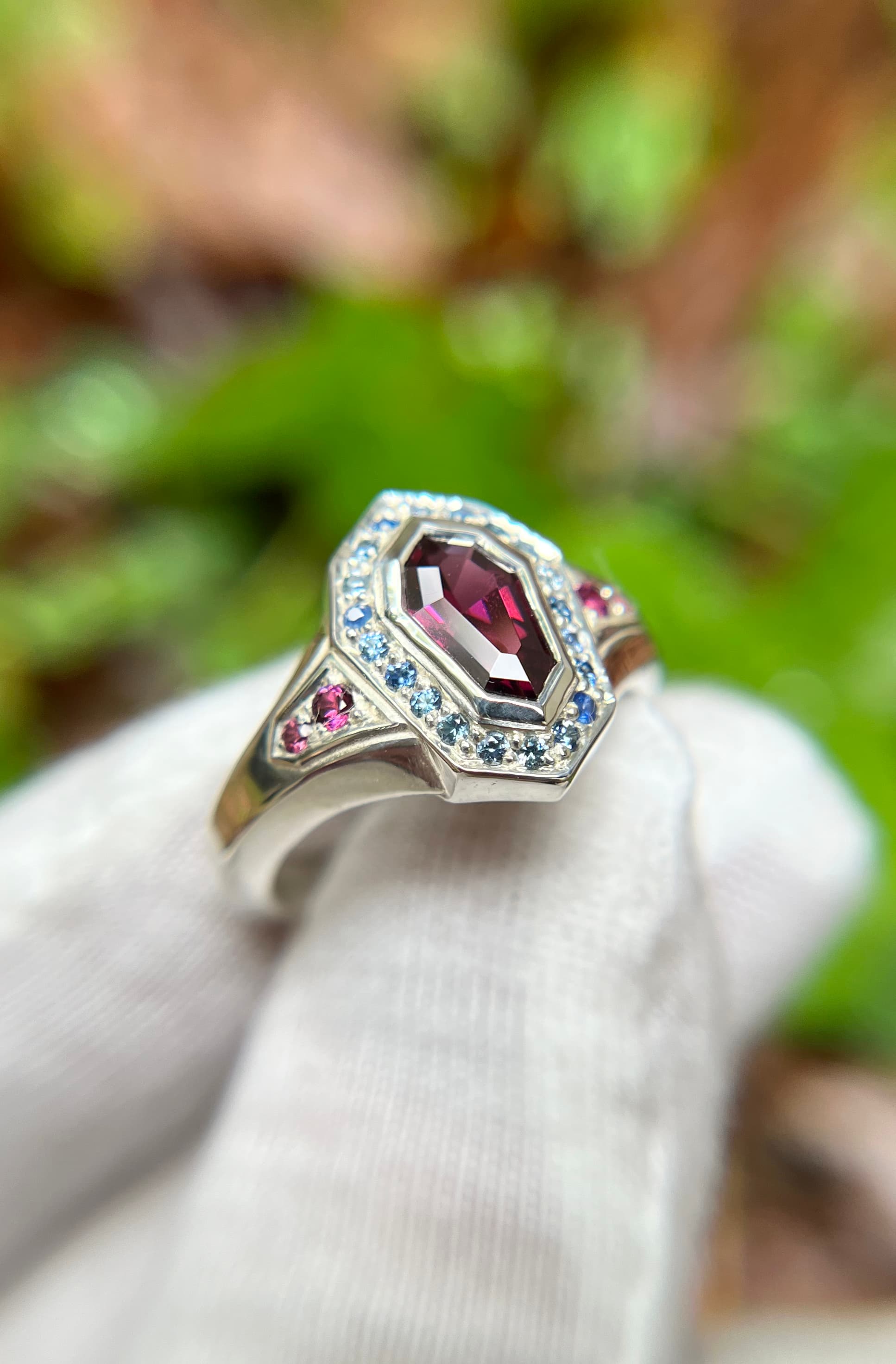 White gold ring with coffin-cut garnet, blue sapphire halo, and pink accent stones